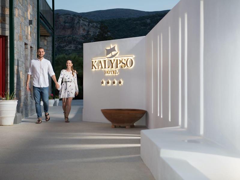 Coppia che cammina vicino al cartello dell'hotel Kalypso con architettura bianca moderna e vista sulla montagna.