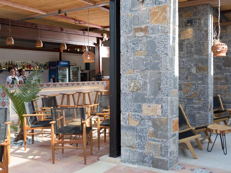 Accogliente caffetteria d'hotel con tavoli e sedie in legno, muro di pietra, piante appese e illuminazione calda.