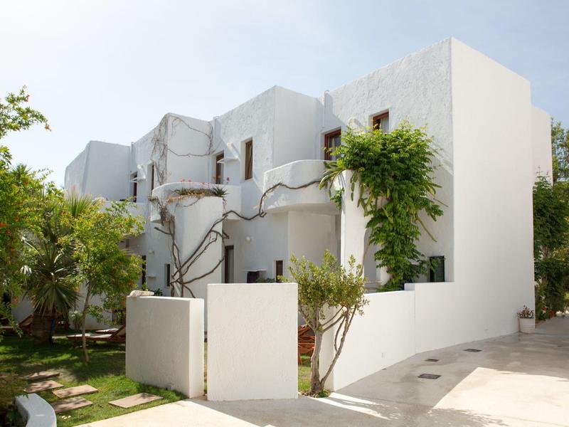 Villa moderna bianca circondata da verde e cielo limpido, con elementi di design minimalista.