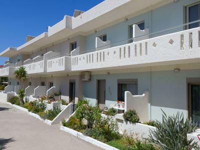 Two-story hotel building with balconies and plants in front of the entrances under clear sky.