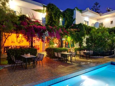 Hotel terrace with illuminated pool, tables, and chairs in front of a plant-covered facade at night.