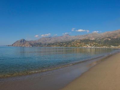 Mare blu limpido con spiaggia sabbiosa e montagne sullo sfondo sotto un cielo limpido.