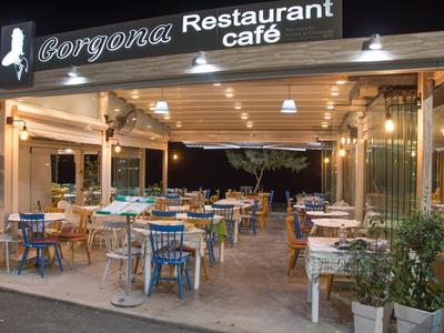 Ristorante caffè aperto con tavoli e sedie, circondato da piante e illuminato alla sera.
