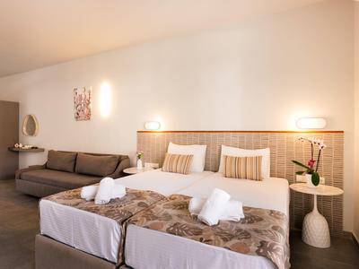 Camera d'hotel con due letti singoli, divano e moderne lampade da parete con luce calda.