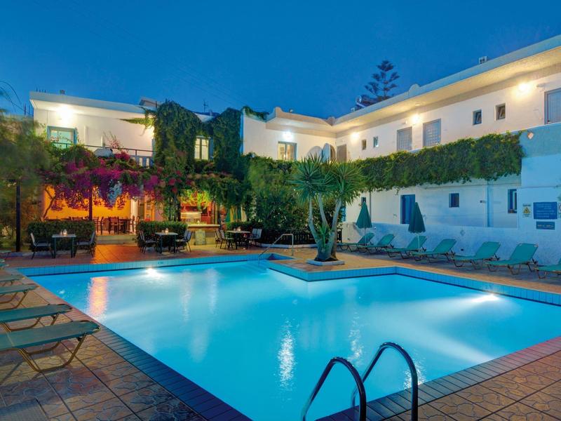 Area piscina illuminata con lettini e edifici dell'hotel circostanti di notte.