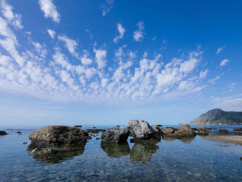 Mare limpido con rocce sotto un cielo azzurro punteggiato di nuvole.