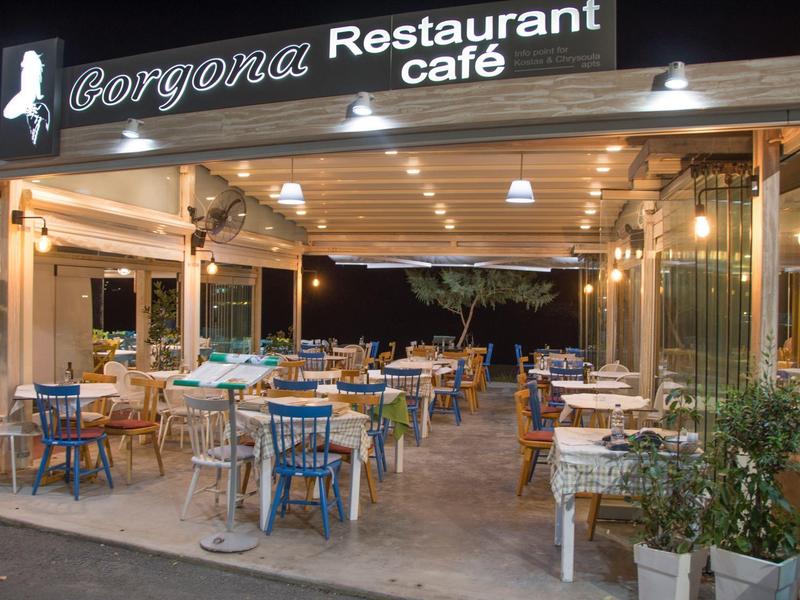 Ristorante caffè aperto con tavoli e sedie, circondato da piante e illuminato alla sera.