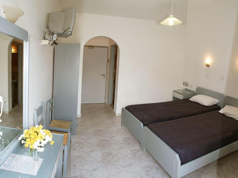 Camera d'hotel semplicemente arredata con due letti singoli, pavimento spazioso e pareti chiare.