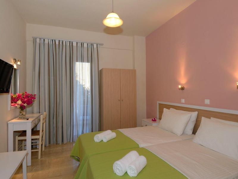 Camera d'hotel con letto matrimoniale, coperte verdi, asciugamani bianchi e scrivania accanto a una finestra con tende.