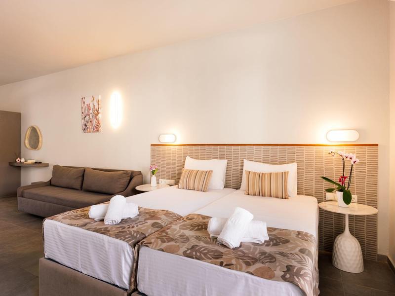 Camera d'hotel con due letti singoli, divano e moderne lampade da parete con luce calda.