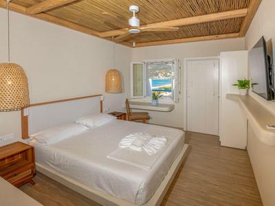 Helles Hotelzimmer mit Doppelbett, Holzmöbeln, Deckenventilator und Blick aus dem Fenster.