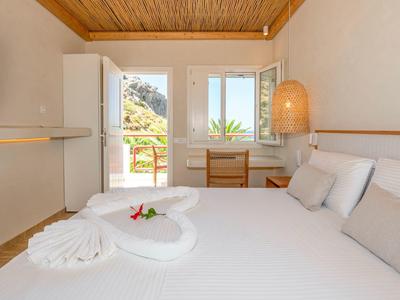 Helles Hotelzimmer mit weißem Bett, Vorsatz im Schwan-Design und Blick auf Outdoor-Balkon.