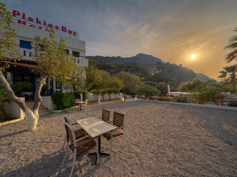 Freiluftbereich mit Holztisch und Stühlen vor einem Gebäude, umliegende Berge und Sonnenuntergang.