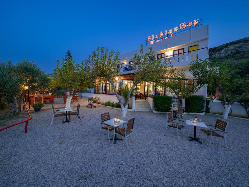 Freiluftrestaurant mit Tischen und Stühlen auf Kiesfläche vor beleuchtetem Gebäude am Abend.