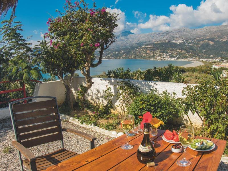 Garten mit Holztisch, Stuhl, Weinkaraffe, Gläsern und Blick auf grüne Hügel und blauen Himmel.
