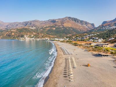 Una spiaggia tranquilla con ombrelloni, acqua blu e montagne sullo sfondo.