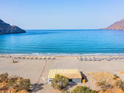 Ampia spiaggia di sabbia con ombrelloni davanti a mare calmo e montagne sullo sfondo.