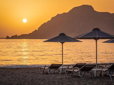 Playa con tumbonas y sombrillas al atardecer con montañas al fondo