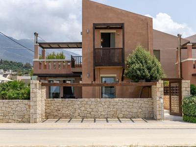 Casa vacanze moderna con terrazza e muro di pietra davanti a prato verde sotto cielo azzurro.