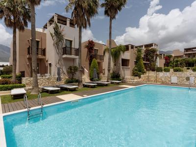 Piscina clara con tumbonas y palmeras frente a un edificio hotelero moderno en un día soleado.