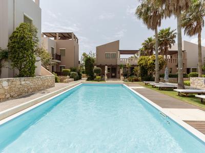 Área de piscina moderna con agua azul clara, rodeada de edificios hoteleros y palmeras.