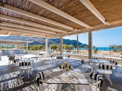 Terraza abierta de un restaurante con mesas y sillas, vista al mar y montañas.