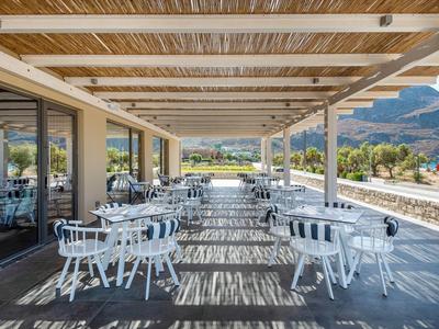 Terrazza coperta con sedie e tavoli bianchi con vista su montagne e mare.