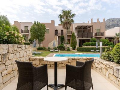 Terrazza con tavolo e sedie di fronte a una piscina e case vacanze mediterranee.