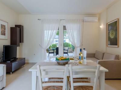 Soggiorno luminoso con zona pranzo, divano, TV e vista su una terrazza attraverso porte in vetro.