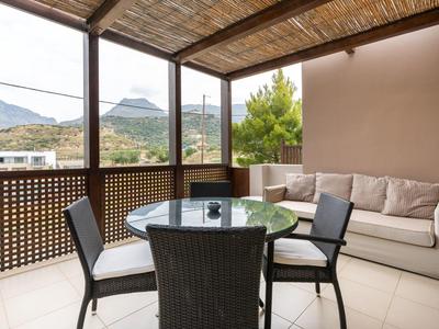 Accogliente terrazza con tavolo in vetro, sedie e divano con vista su montagne e natura.
