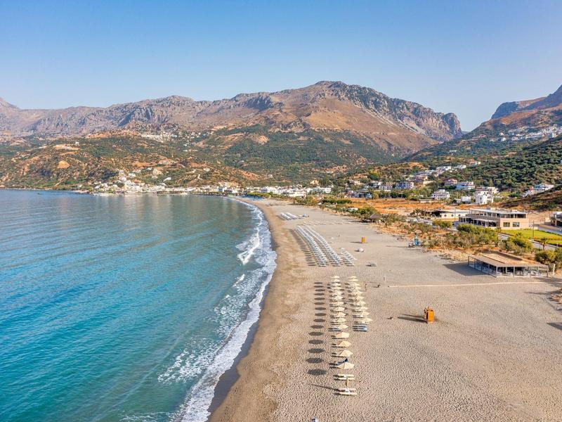 Una spiaggia tranquilla con ombrelloni, acqua blu e montagne sullo sfondo.