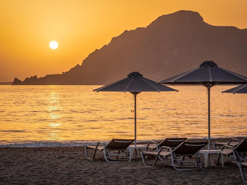 Spiaggia con lettini e ombrelloni al tramonto davanti alle montagne.