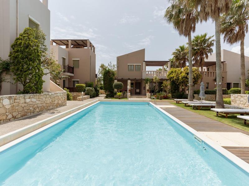 Piscina moderna dell'hotel con acqua limpida e blu, circondata da palme e edifici beige.