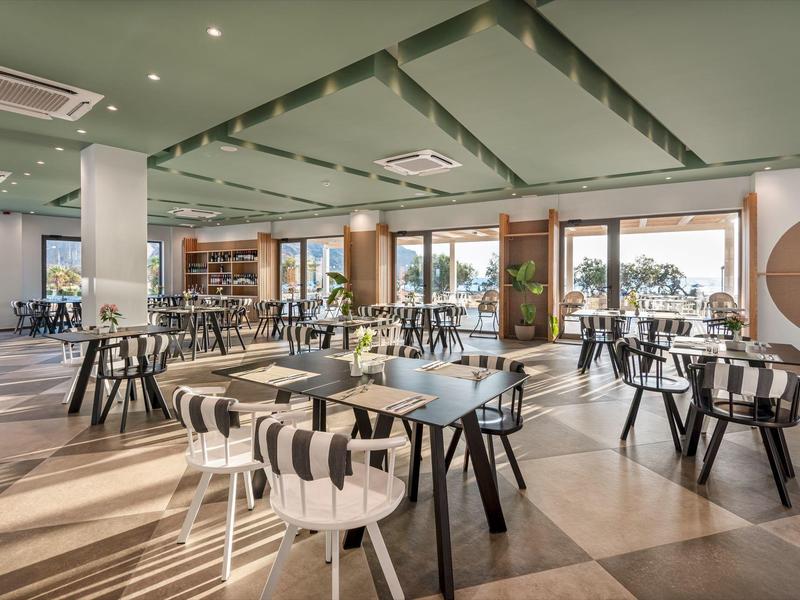 Ristorante luminoso e moderno con sedie bianche e nere e tavoli in legno, grandi finestre con vista.