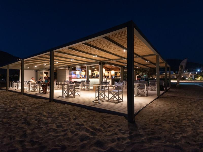 Padiglione sulla spiaggia illuminato con posti a sedere di notte, circondato dalla sabbia.