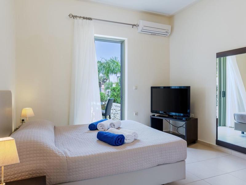 Camera luminosa con letto matrimoniale, asciugamano blu, TV e grande specchio accanto alla porta.