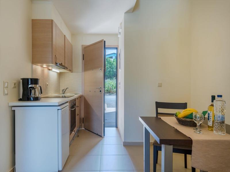 Angolo cottura compatto con macchina da caffè, frigorifero e tavolo da pranzo in una stanza luminosa.