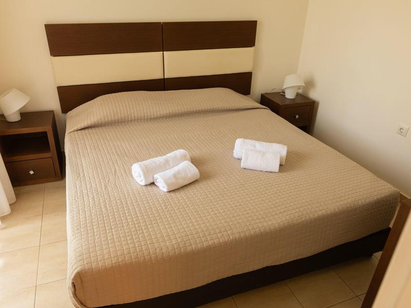 Camera d'hotel semplice con letto matrimoniale, biancheria marrone-beige e due asciugamani arrotolati.