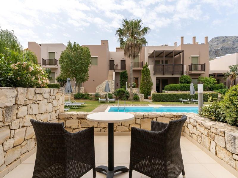 Terrazza con tavolo e sedie di fronte a una piscina e case vacanze mediterranee.