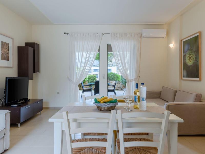 Soggiorno luminoso con zona pranzo, divano, TV e vista su una terrazza attraverso porte in vetro.