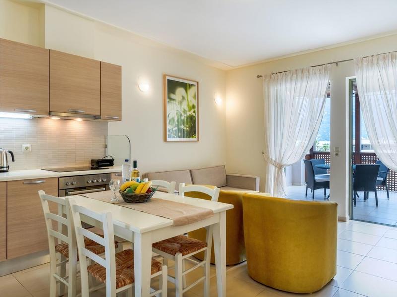 Sala da pranzo luminosa con mobili in legno, tavolo bianco, divano giallo e accesso al balcone