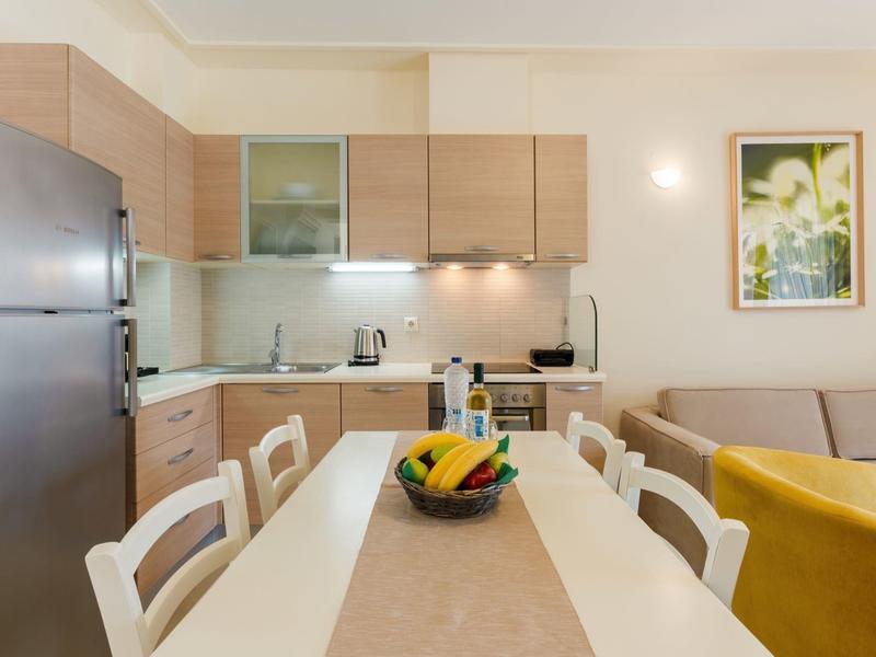 Cucina luminosa con mobili in legno, tavolo da pranzo con cestino di frutta e angolo relax sullo sfondo.