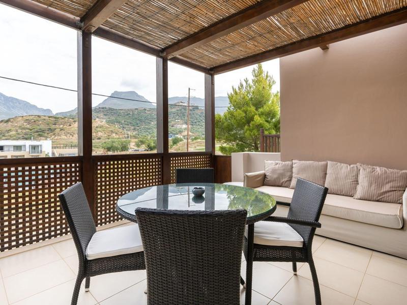 Accogliente terrazza con tavolo in vetro, sedie e divano con vista su montagne e natura.