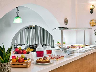 Buffet avec gâteaux, fruits et boissons dans une pièce lumineuse avec plafond voûté et plantes.