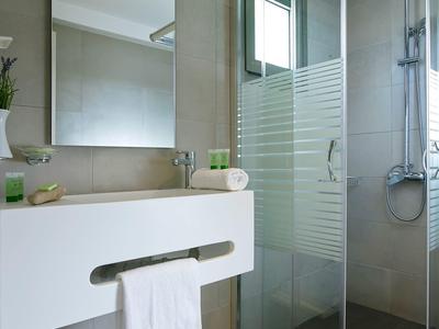 Salle de bain moderne avec douche, lavabo et serviettes dans une chambre d'hôtel.