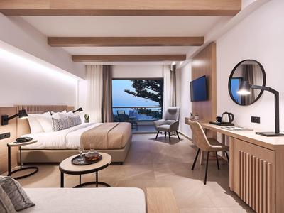 Chambre d'hôtel moderne avec lit double, coin salon, bureau et vue sur la mer à travers de grandes fenêtres.