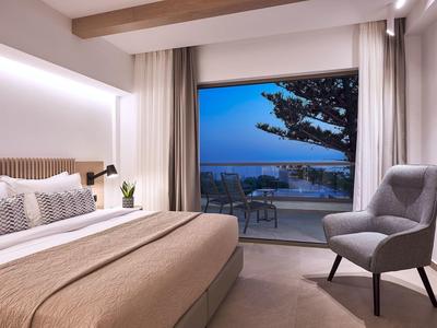 Chambre d'hôtel moderne avec grand lit, fauteuil et vue sur la mer au crépuscule