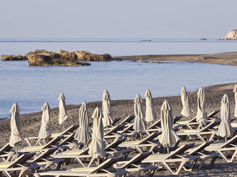 Parasols fermés et chaises longues sur une plage de sable vide avec une mer calme en arrière-plan.