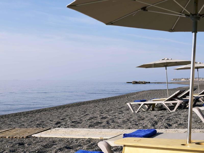 Plage avec chaises longues et parasols au bord de la mer calme par une journée claire.