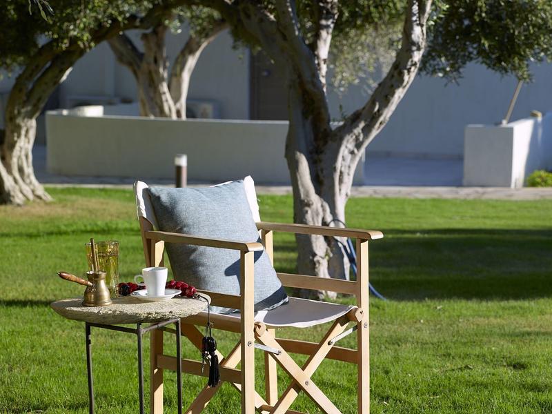 Une chaise avec coussins à côté d'une petite table avec café et pâtisserie dans le jardin.